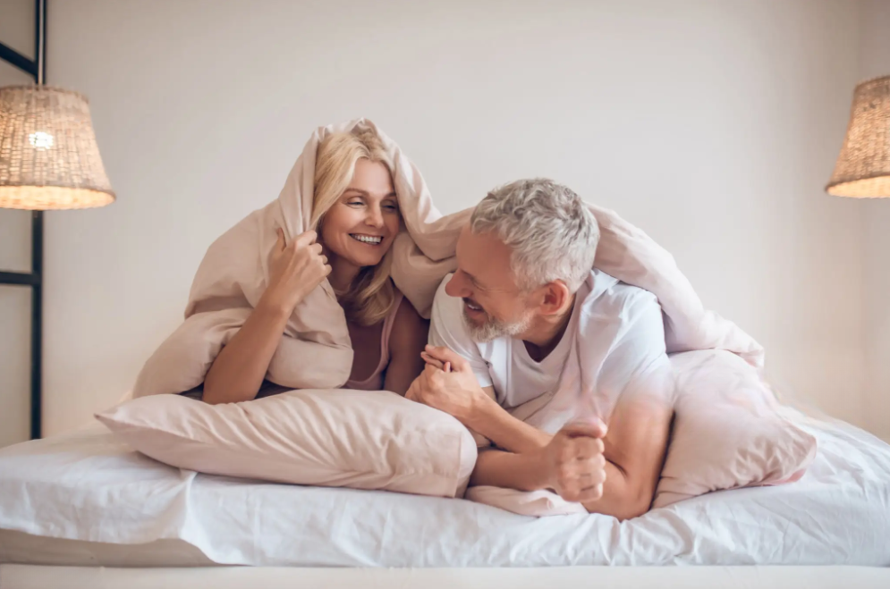 A man and woman are comfortably lying together on a bed, sharing a moment of relaxation and intimacy. After using the Dr Joel Kaplan Pump System